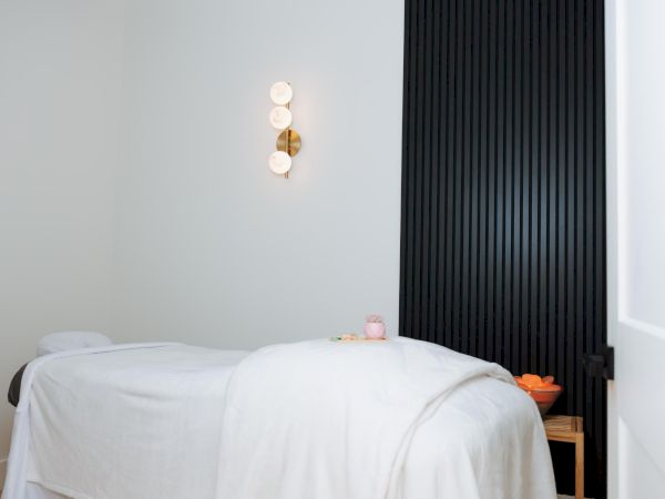A serene massage or spa treatment room with a white massage table, soft lighting, and a black slatted wall accent.