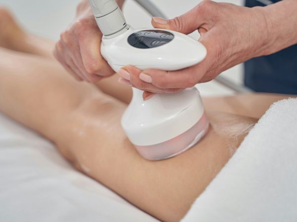 A medical device is used on a person&rsquo;s abdomen or thigh, likely performing a non-invasive body treatment or ultrasound therapy, with a clinician operating the handheld wand.