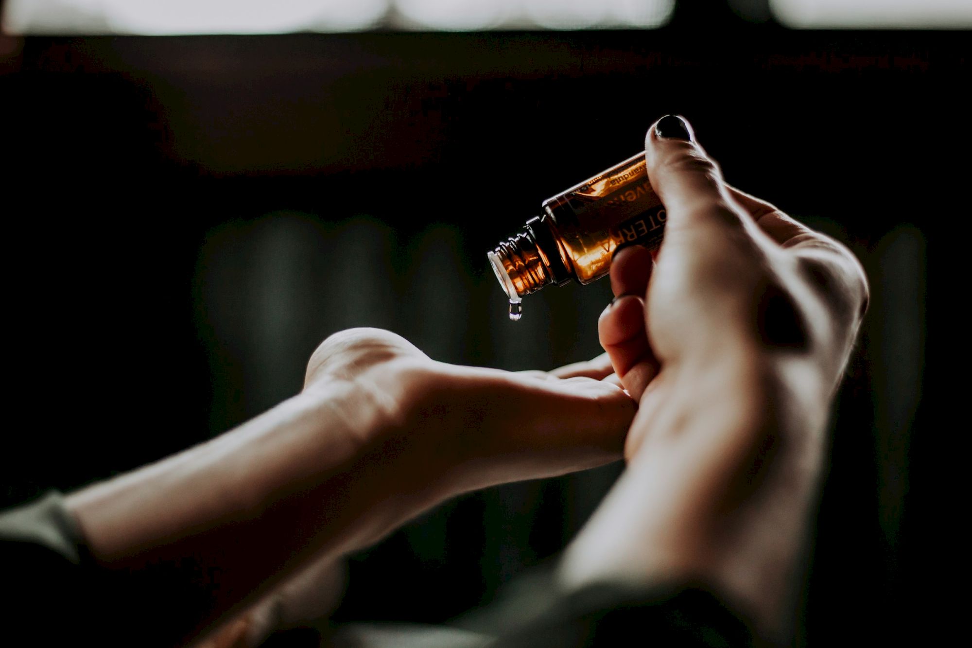 A person pours oil from a small amber bottle onto their hand in a dimly lit setting.