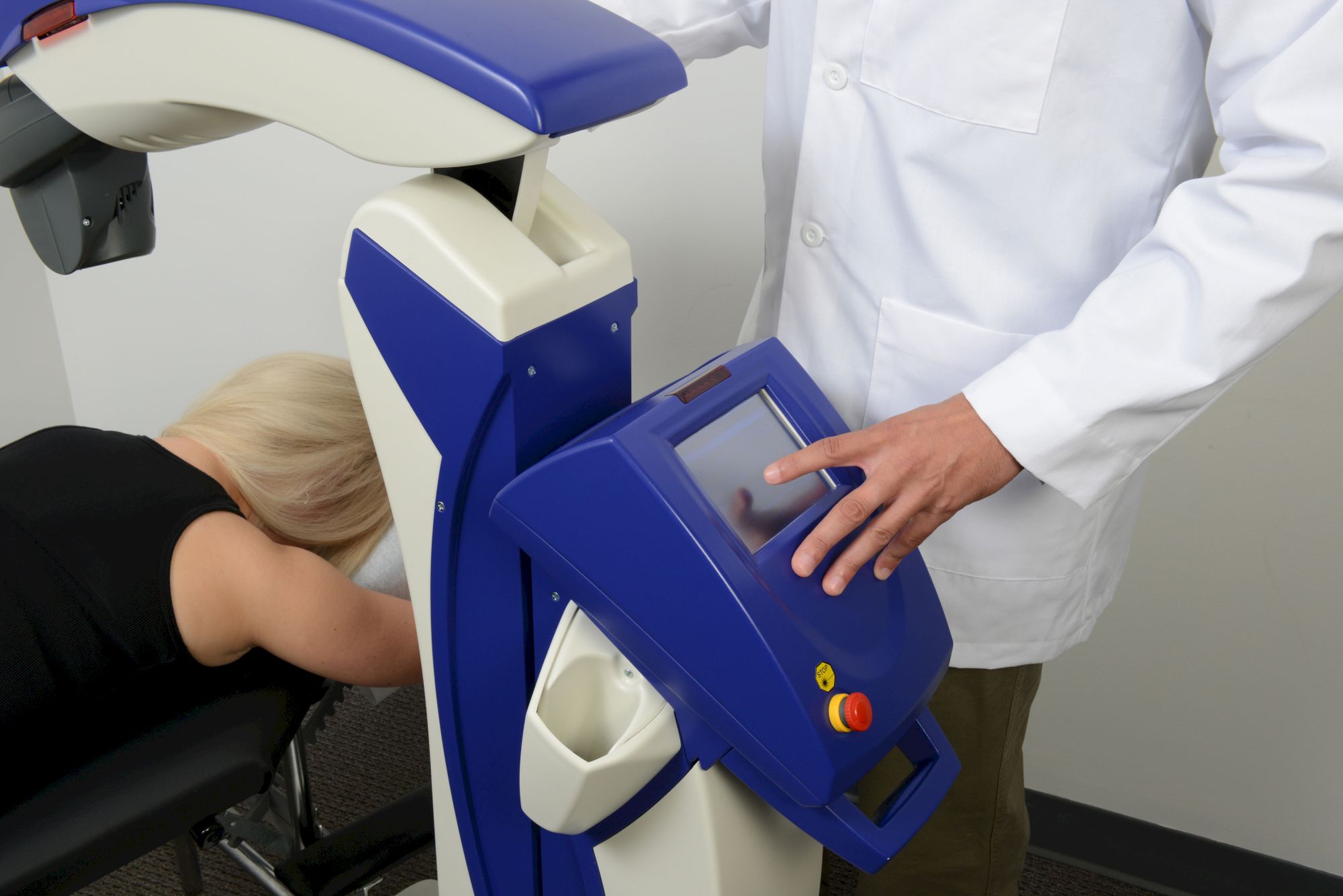 A person is using an eye examination machine operated by a professional in a white coat, with a touch screen interface visible.