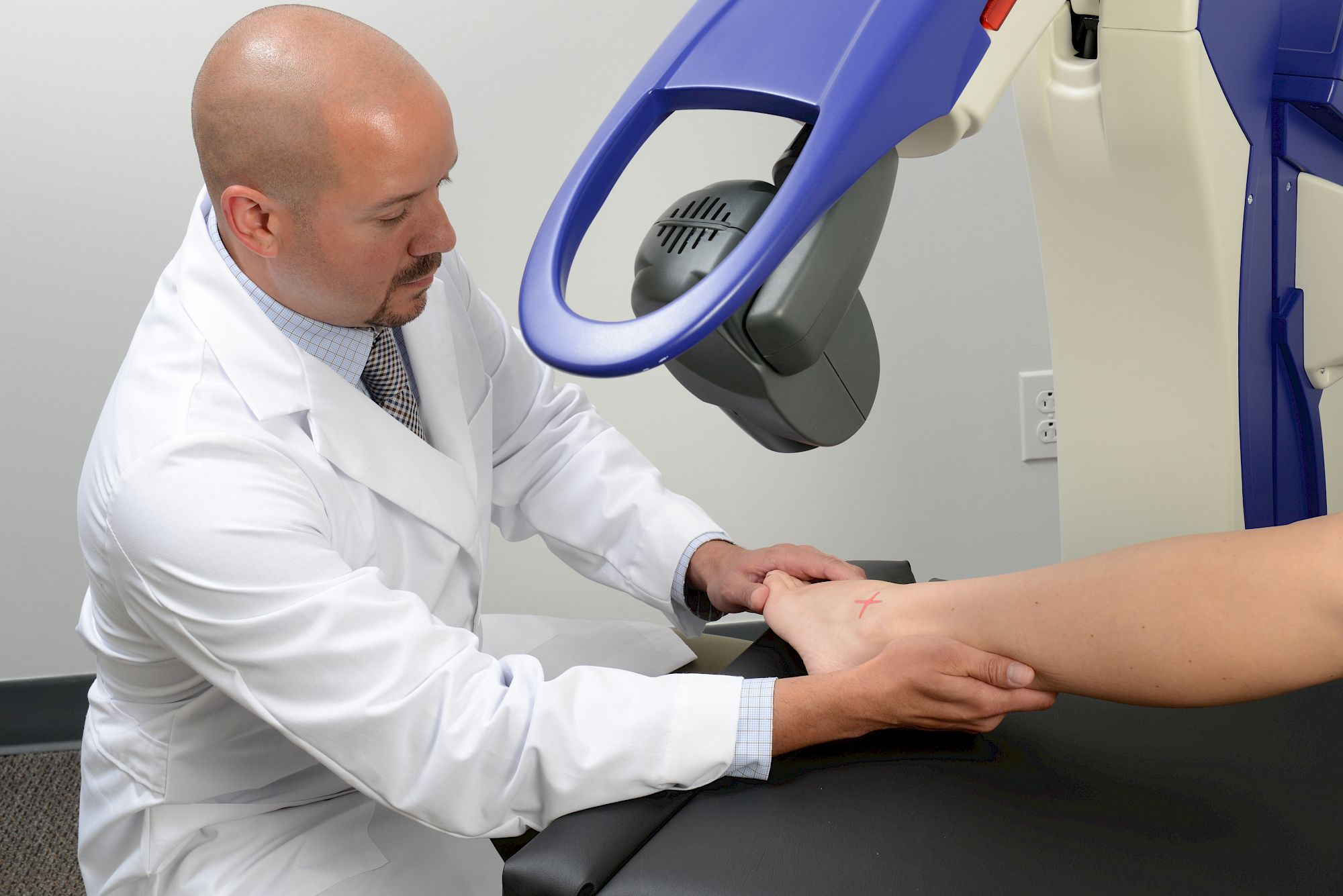 A medical professional examines a patient's wrist using specialized equipment in a clinical setting.