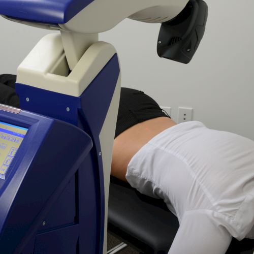 A person is lying on a medical device, possibly for therapy, with a computer screen displaying information nearby.