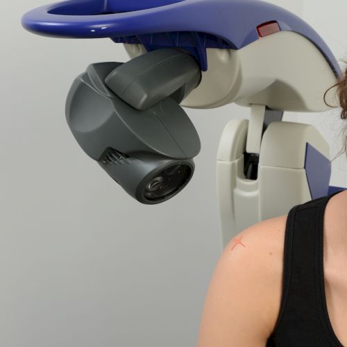 A person near a massage or therapy device aimed at their shoulder area, with part of the equipment visible.