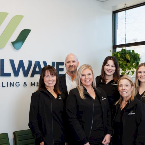 A group of people posing and smiling indoors, behind them a wall with a logo that reads &ldquo;ITALW&hellip;&rdquo; and plants in view, all looking at the camera.