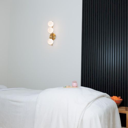 A simple bedroom corner with a white bed, pale blue walls, and a dark floor lamp casting light, creating a calm, minimalist vibe.