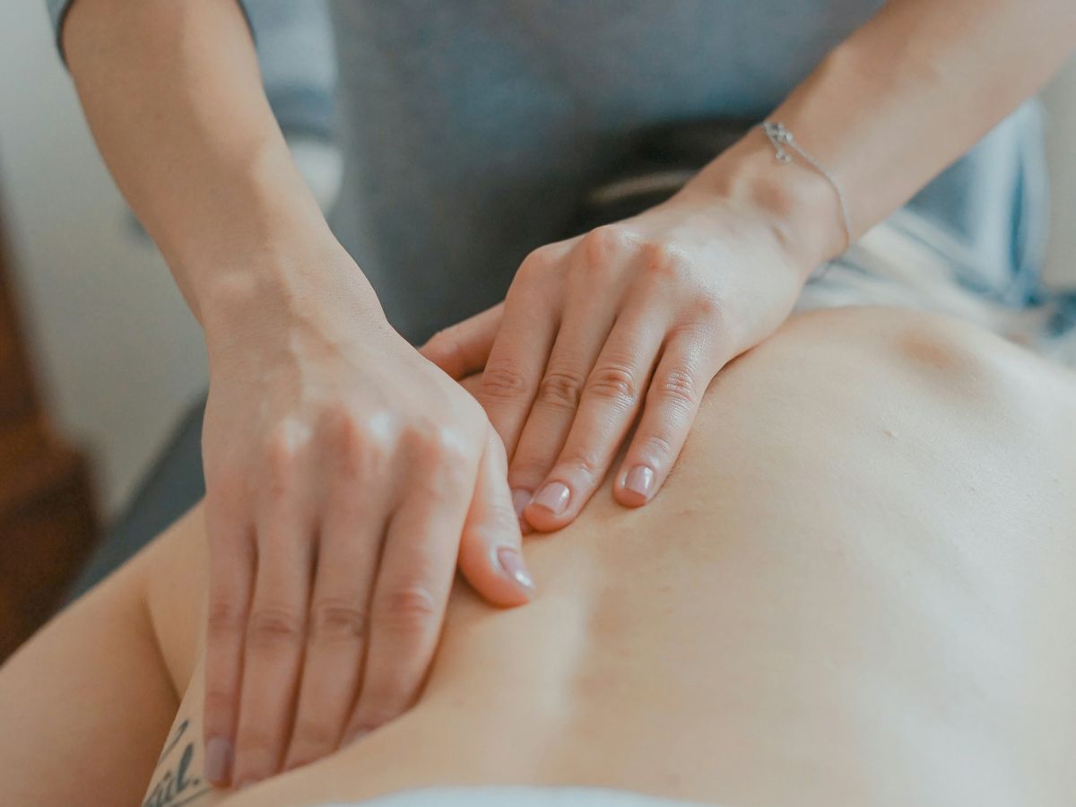 A therapist gently massages a person&rsquo;s bare back and shoulder with soothing hands in a calm wellness setting.